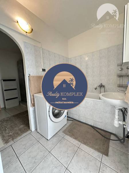 A bathroom in a studio apartment with a washing machine, a sink, and a bathtub on light tiles.