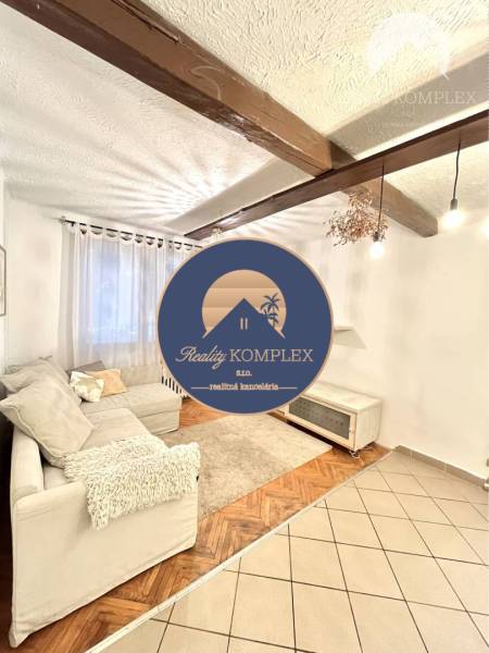 Living room in a three-room apartment with a wooden decor floor and a beamed ceiling.