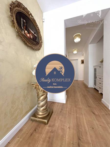 A hallway with a wooden decor floor, a golden stand, and a painting in a family house.