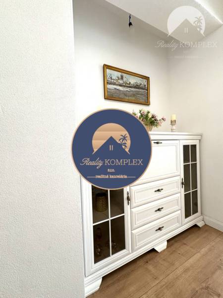 A room with a white dresser, wood-patterned flooring, and a painting on the wall in a family house.
