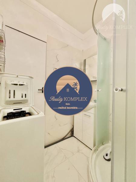 Bathroom in a 2-room apartment with a washing machine, shower, and white sanitary ware.