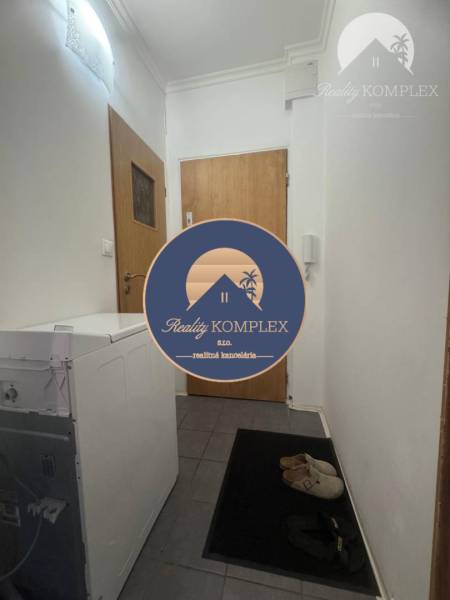 Entrance hallway in a one-room apartment with a washing machine and shoes on dark tiles.