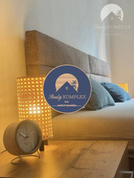 Partial view of a bed in a studio apartment with a lamp and an alarm clock.