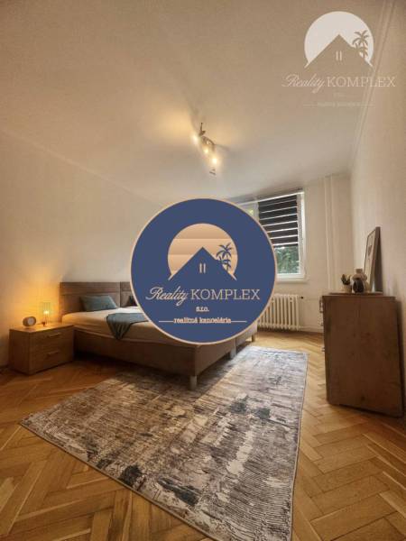 A bright room with a bed, carpet, and wood-patterned flooring in a studio apartment.