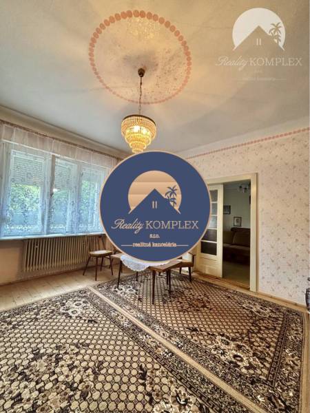 A room in a family house with a carpet, chandelier, and windows offers a cozy space.