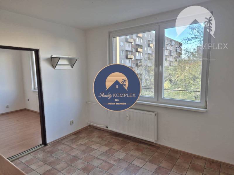 A room with tiled flooring and a spacious window in a studio apartment, next to a floor with a wooden decor.