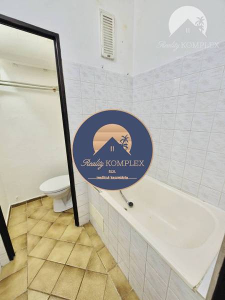 Bathroom in a studio apartment with a bathtub and toilet, tiles in brown shades.