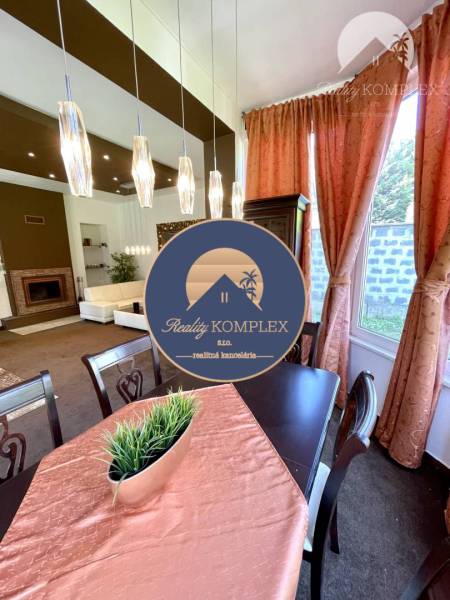 Dining room in a family house with lighting, curtains, and a table with a decorative tablecloth.