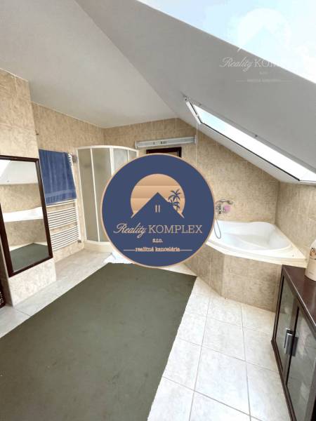 A bathroom in a family house with a bathtub and a shower under a sloped roof.