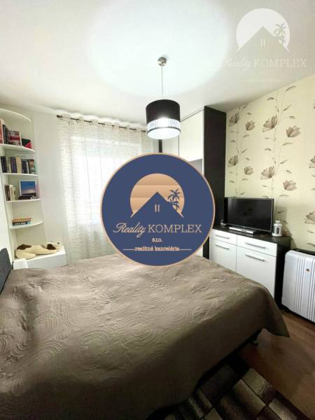 A bedroom in a two-room apartment with a wooden decor floor and floral wallpaper.