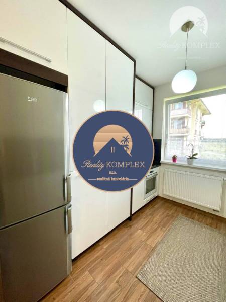 A kitchen in a 2-room apartment with white cabinets, a refrigerator, and a wooden decor floor.