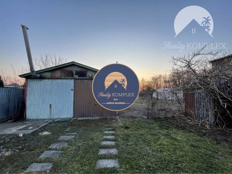 The garden at the family house in Vrakúň with a metal garage and trees, evening sky.