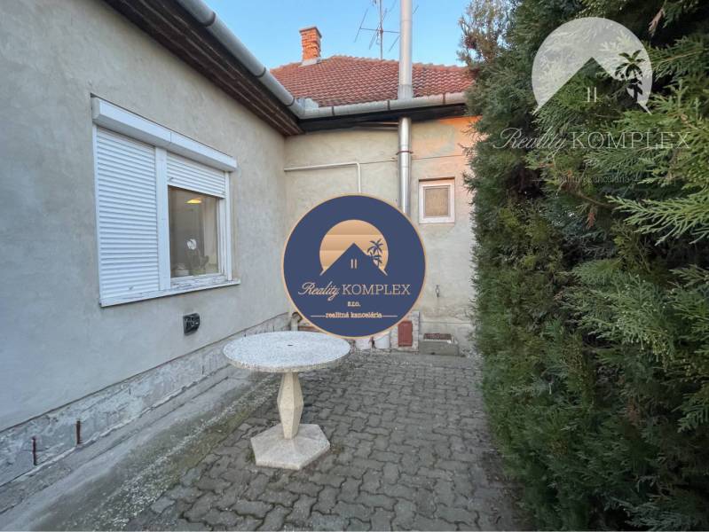 A family house in Vrakúň with a stone table on a paved terrace surrounded by greenery.