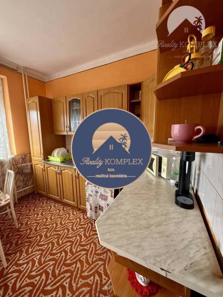 A kitchen in a family house with orange walls, wooden cabinets, and a patterned carpet.