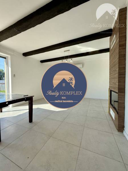 Living room with a fireplace, ceramic floor, and dark ceiling beams in a family house.