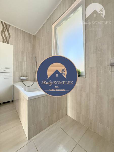 A bathroom with a bathtub and a window in a family house with cream-colored tiles.
