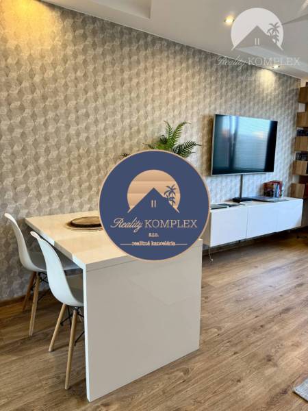 Dining table with white chairs in a 4-room apartment, wooden floor, TV on the wall.