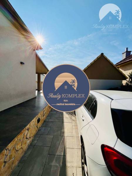 A white car on the driveway, the sun shining on the family house and garden.