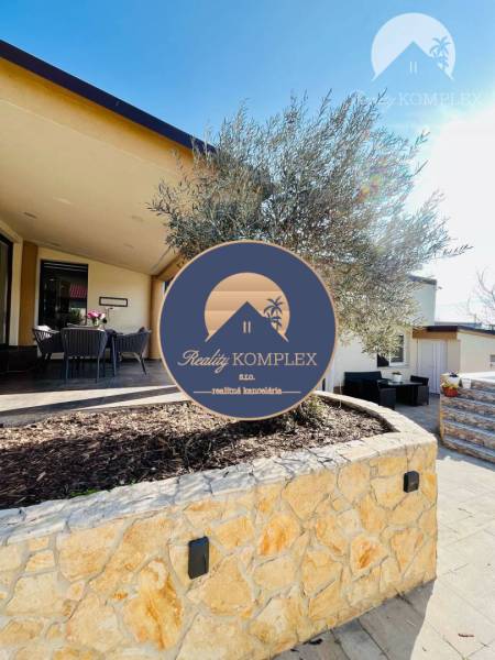 A family house with a terrace and a tree in a stone flower bed in sunny weather.