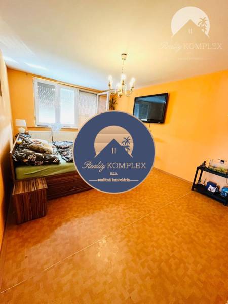 A room in a family house, with orange walls, a chandelier, and a TV on the wall.