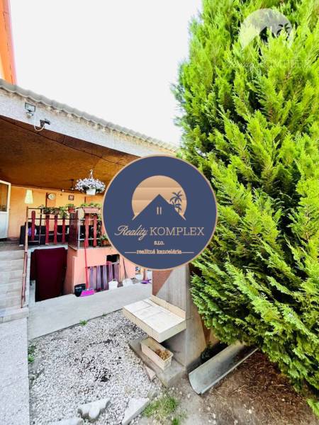 A family house in Okoč with a veranda surrounded by greenery and ornamental planting.