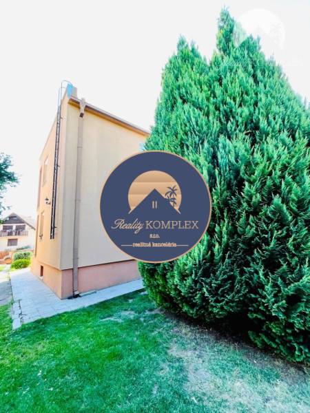 A family house in Okoč with a grassy garden and an adjacent walkway.