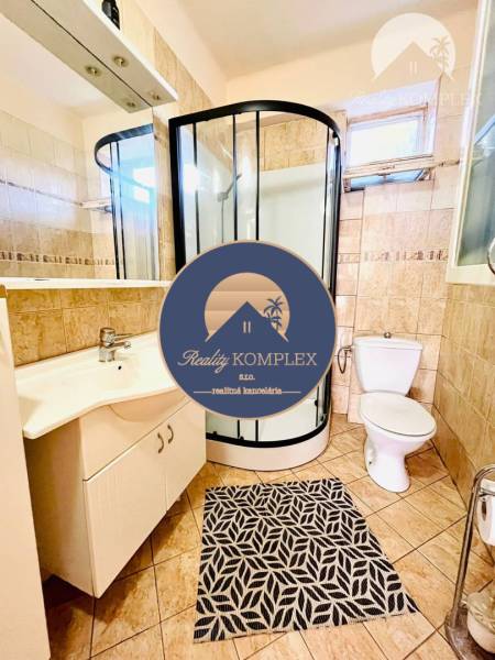 Bathroom in a family house, shower corner, sink, and toilet, tiles with a geometric carpet.