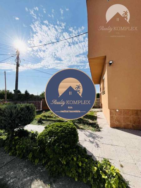A family house in Okoč with a landscaped garden, sunny weather, sky with clouds.