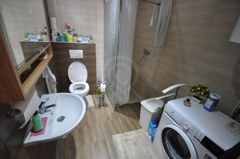 Bathroom in a 2-room apartment with a shower and a washing machine, floor with wood decor.