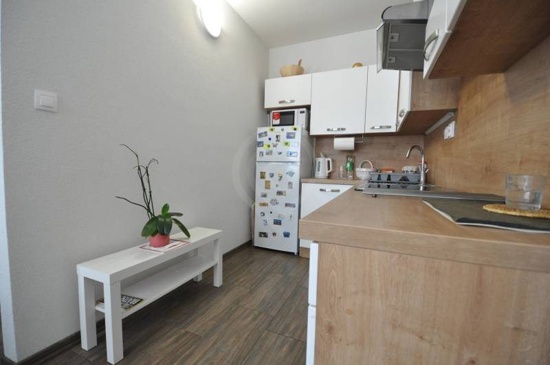 A kitchen in a 2-room apartment with a wooden decor floor and white furniture.