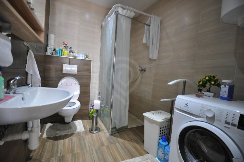 Bathroom in a 2-room apartment with a washing machine and a shower, floor with wood decor.