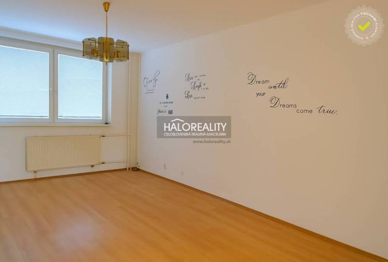 Empty room with a wall with inscriptions and a floor with wooden decor in a 4-room apartment.