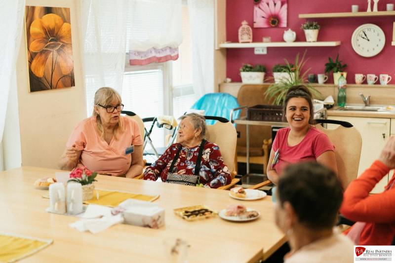 A group of people indoors discussing around a table with food and drinks.