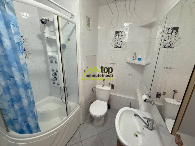 Bathroom with a bathtub, sink, and toilet in a 2-room apartment, white tiles, blue shower curtain.