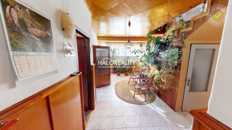 Interior of a family house with plants, chairs, a calendar, and wooden wall decorations.