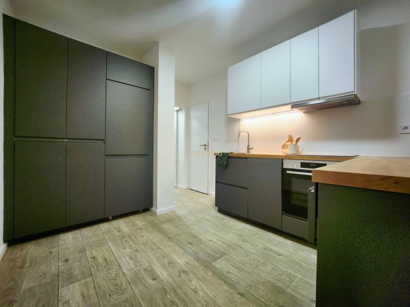 A kitchen in a 2-room apartment with a wood-patterned floor and white and dark gray cabinets.