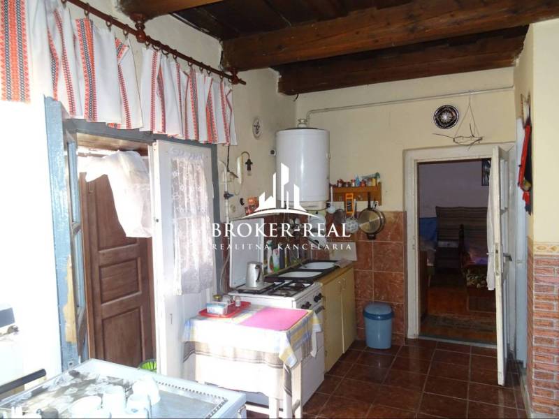 A kitchen in a family house with wooden ceilings, tiles, and curtains.