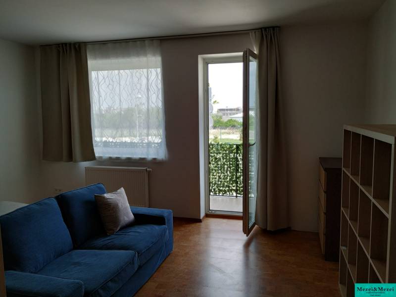 Living room with a blue sofa and an open balcony, complemented by a wood-patterned floor.
