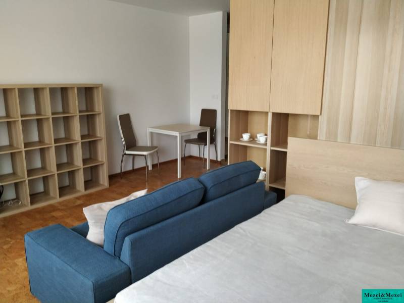 Bright living area with a blue sofa, desk, and shelves in a studio apartment.