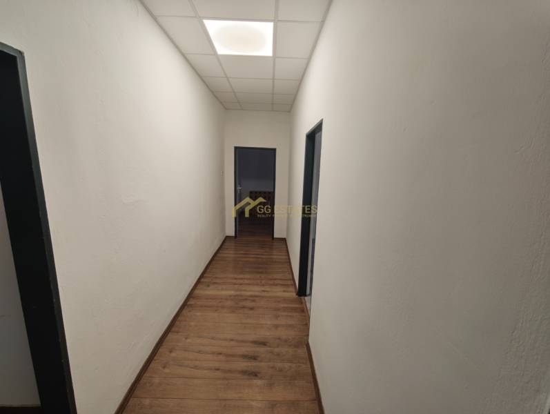 A hallway in an office with white walls and a wooden decor floor.