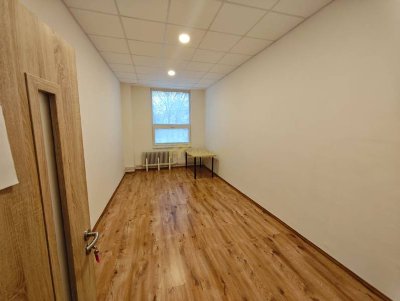 An office with white walls and a wooden decor floor, a simple desk, and a window.