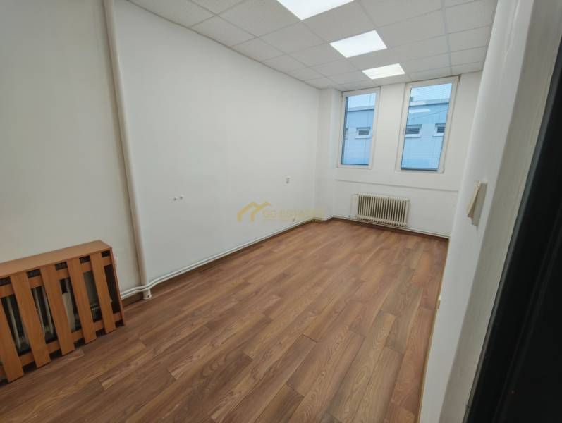 Empty office spaces with wood-patterned flooring and two windows.