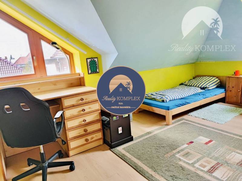 Attic room with a desk, bed, and wooden decor flooring in a family house.