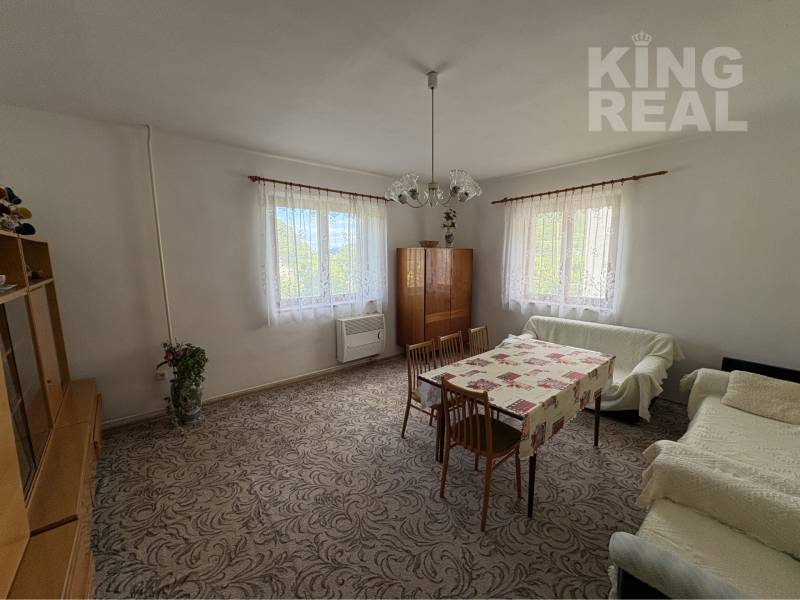 Living room in a family house with carpet flooring, wooden furniture, and large windows.