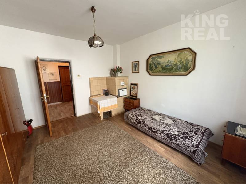 A room in a family house with a wooden decor floor, a bed, and a picture on the wall.