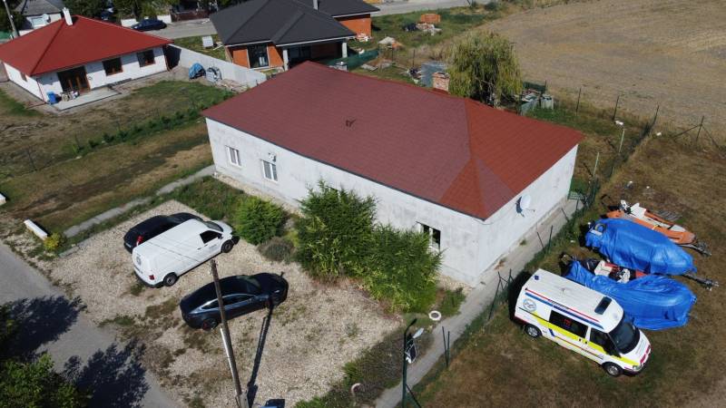 A family house in Zemianska Olča with cars parked on a gravel lot and covered equipment.