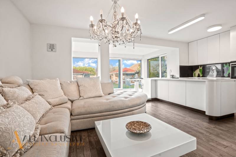 Living room of a family house with a sofa, chandelier, and kitchen unit, floor with wood decor.
