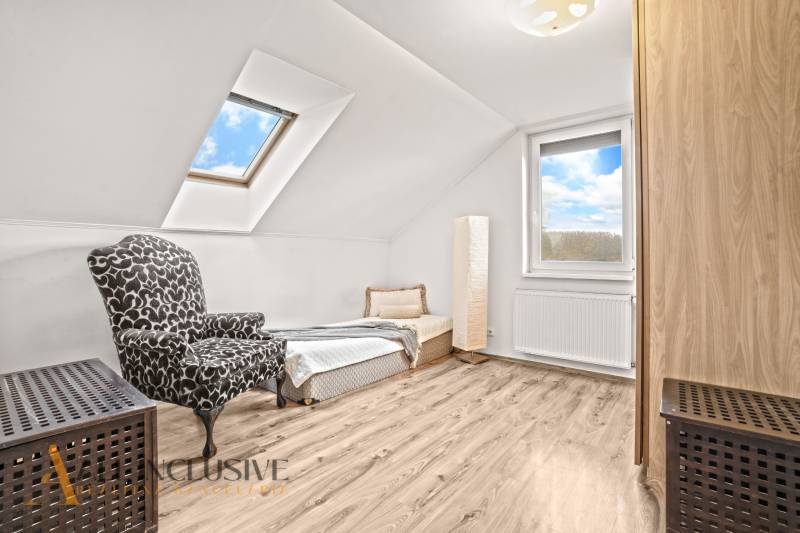Attic room in a family house with an armchair, bed, and wooden decor flooring.