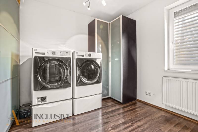 Laundry room in a family house with a washing machine, dryer, and wooden decor flooring.