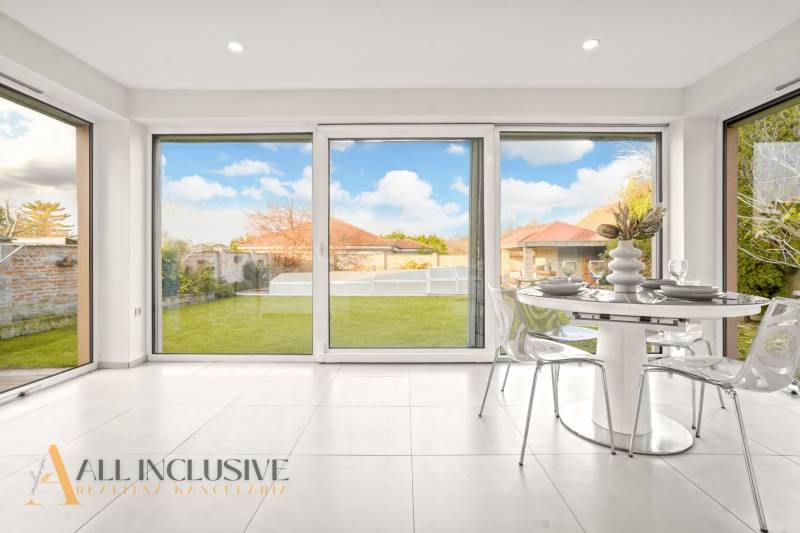 The interior of a family house with a dining nook, glass doors to the garden, and a white floor.